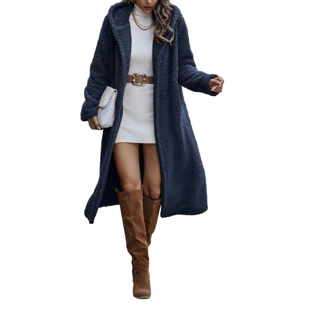 Woman wearing a long navy coat, white dress, and brown knee-high boots on a city street.