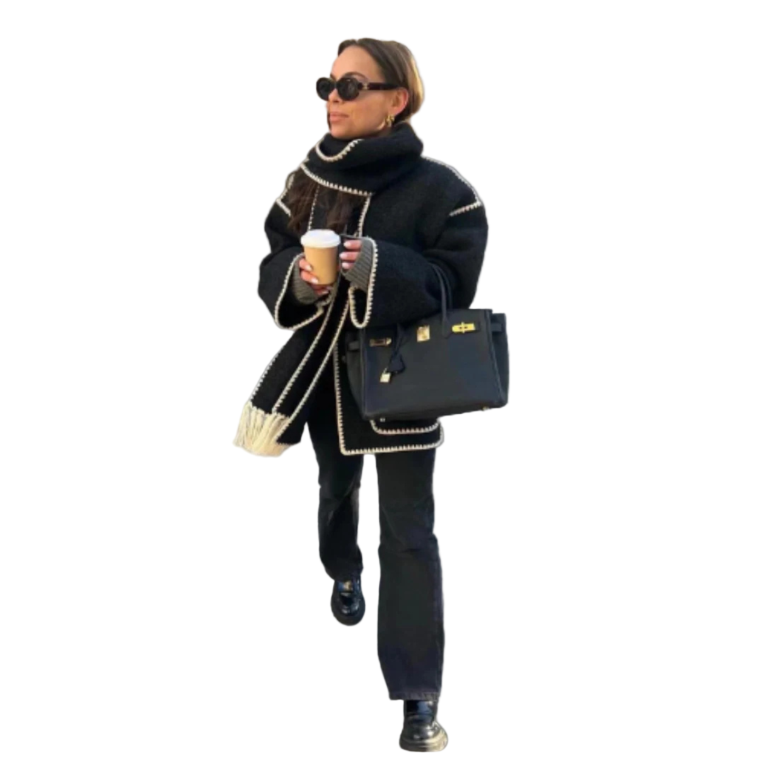 Woman in black outfit with white accents walking outdoors holding a coffee cup.