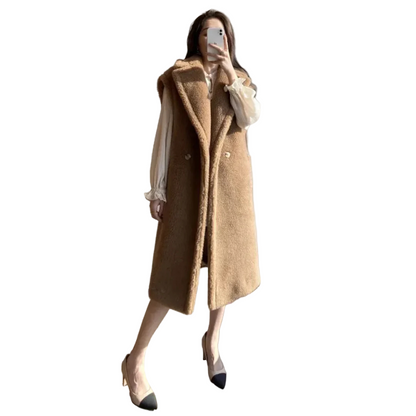 Person wearing a long brown coat in a room with a window.